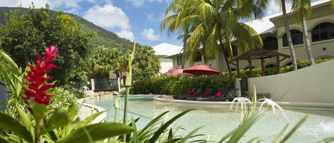 A pool area with palm trees, a gazebo, and a mountain in the background.