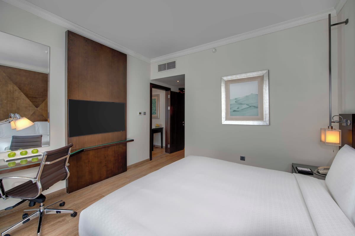 A hotel room with a large bed, a desk with a chair, a mirror, and a framed picture on the wall.