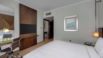 Habitación de hotel con una cama grande, un escritorio con silla, un espejo y un cuadro en la pared.