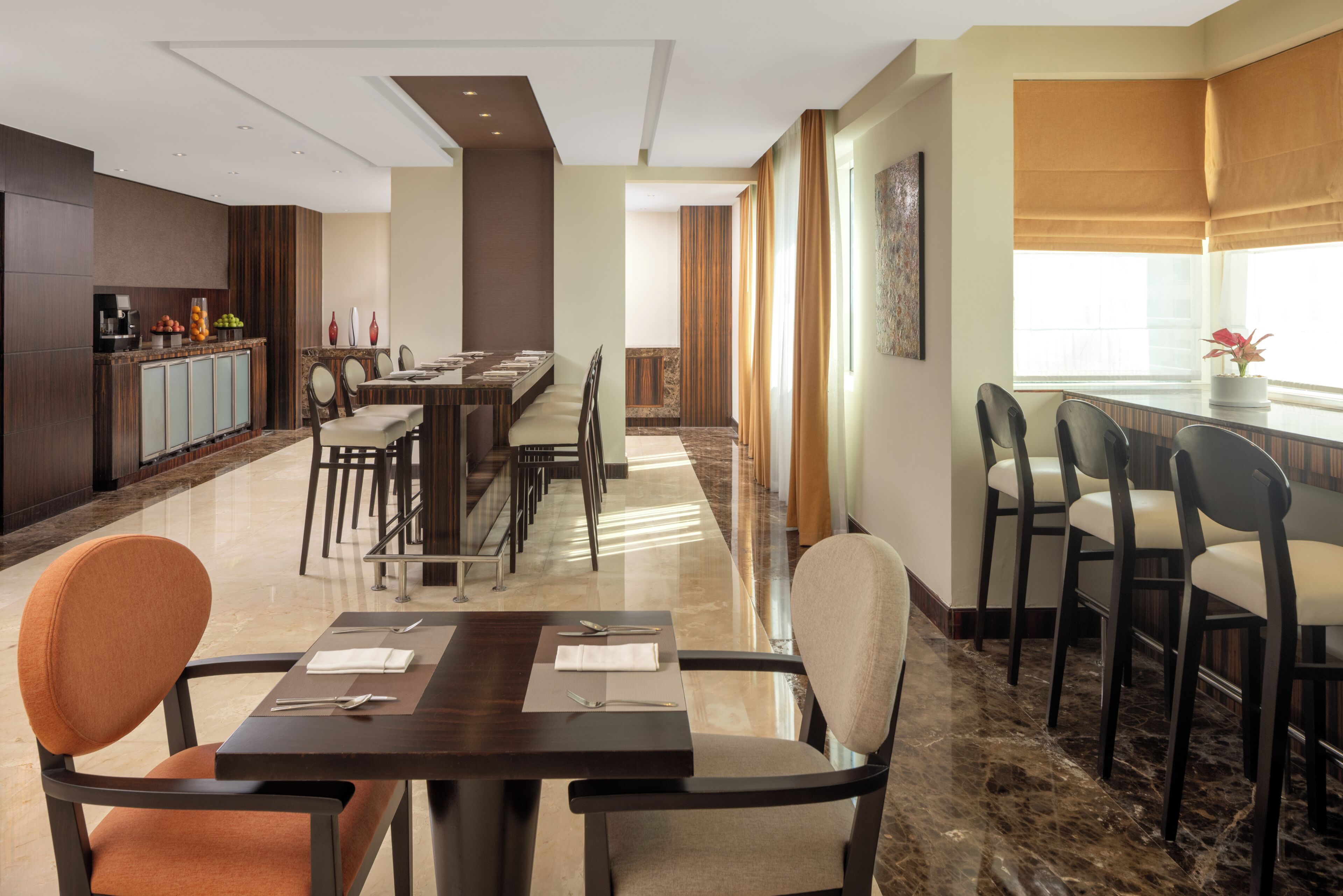 Un espace de restauration d’hôtel comprenant plusieurs tables et chaises, un coin cuisine et une vue sur la ville.