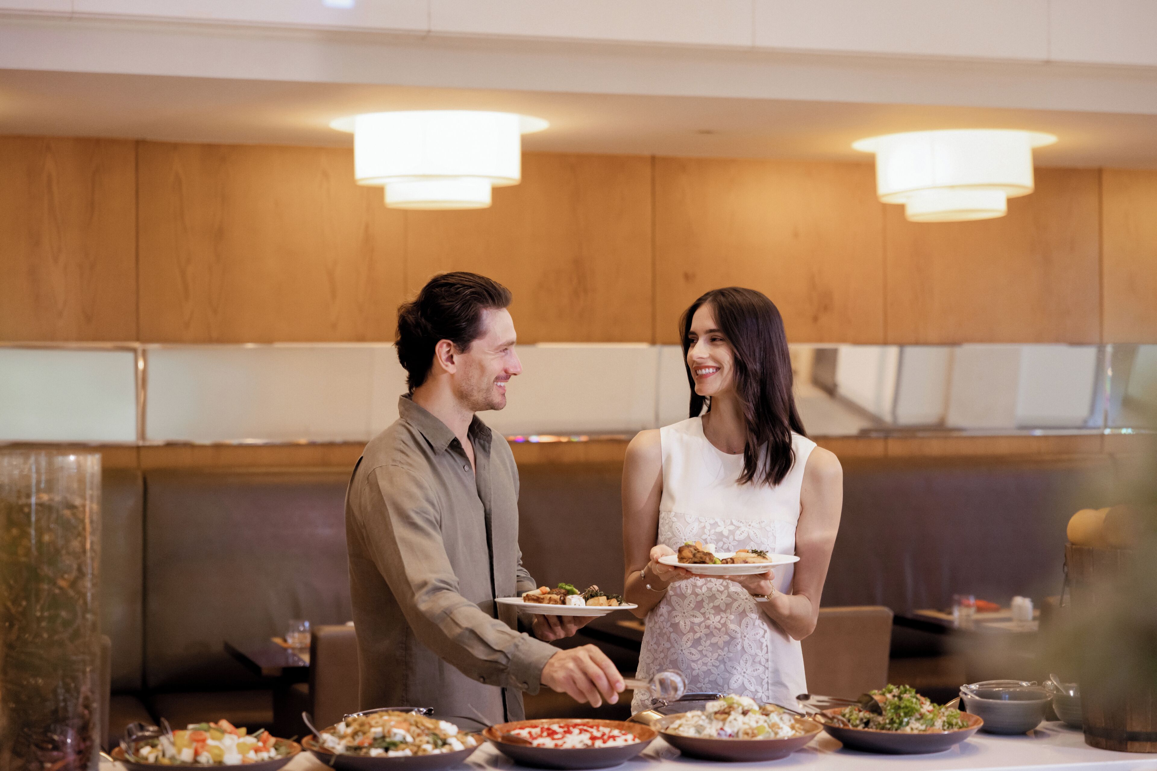 A couple serving themselves at a buffet with various dishes.