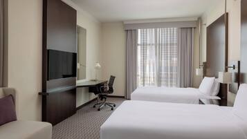 A hotel room with two beds, a desk, a TV, and a window with curtains.