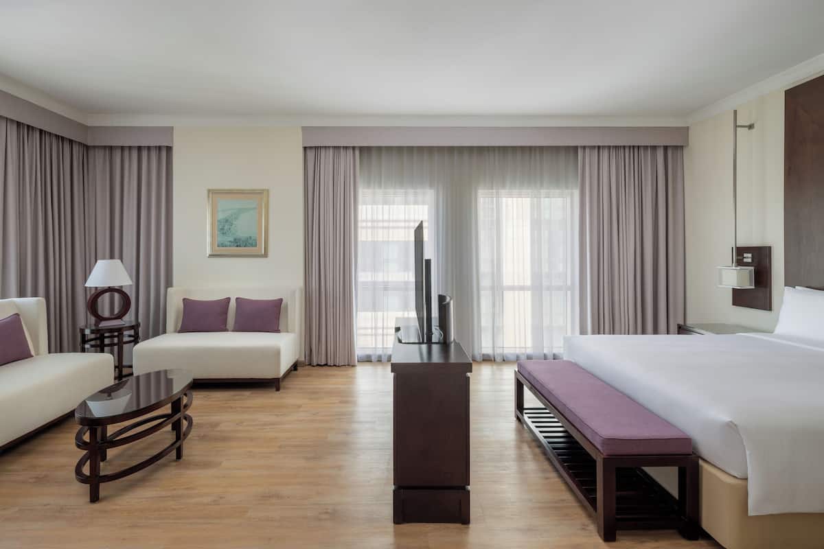 A hotel room with a bed, two sofas, a coffee table, a TV, and a painting on the wall.