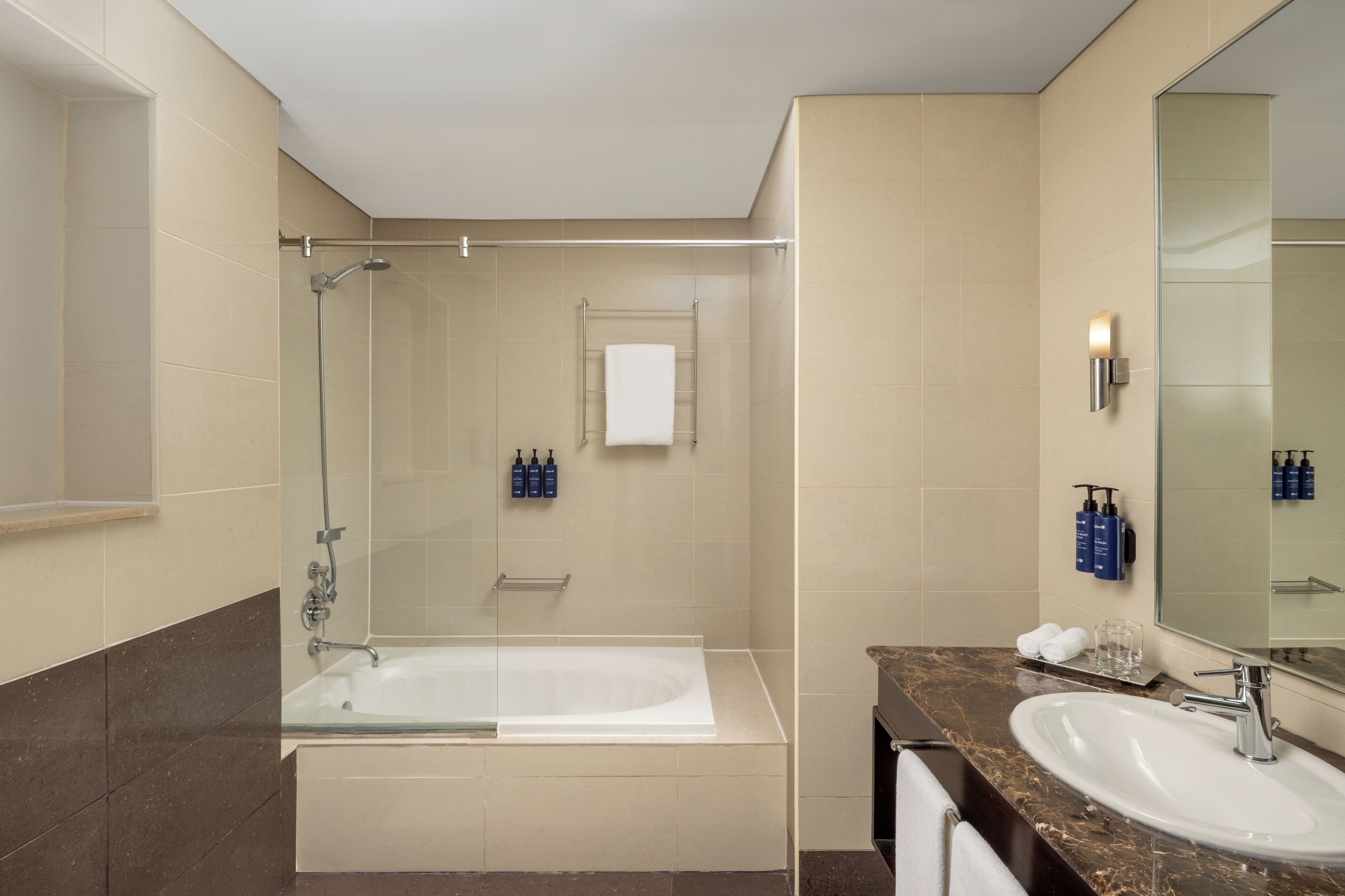 A modern bathroom with a glass-enclosed shower, a white bathtub, a marble countertop, and a large mirror.