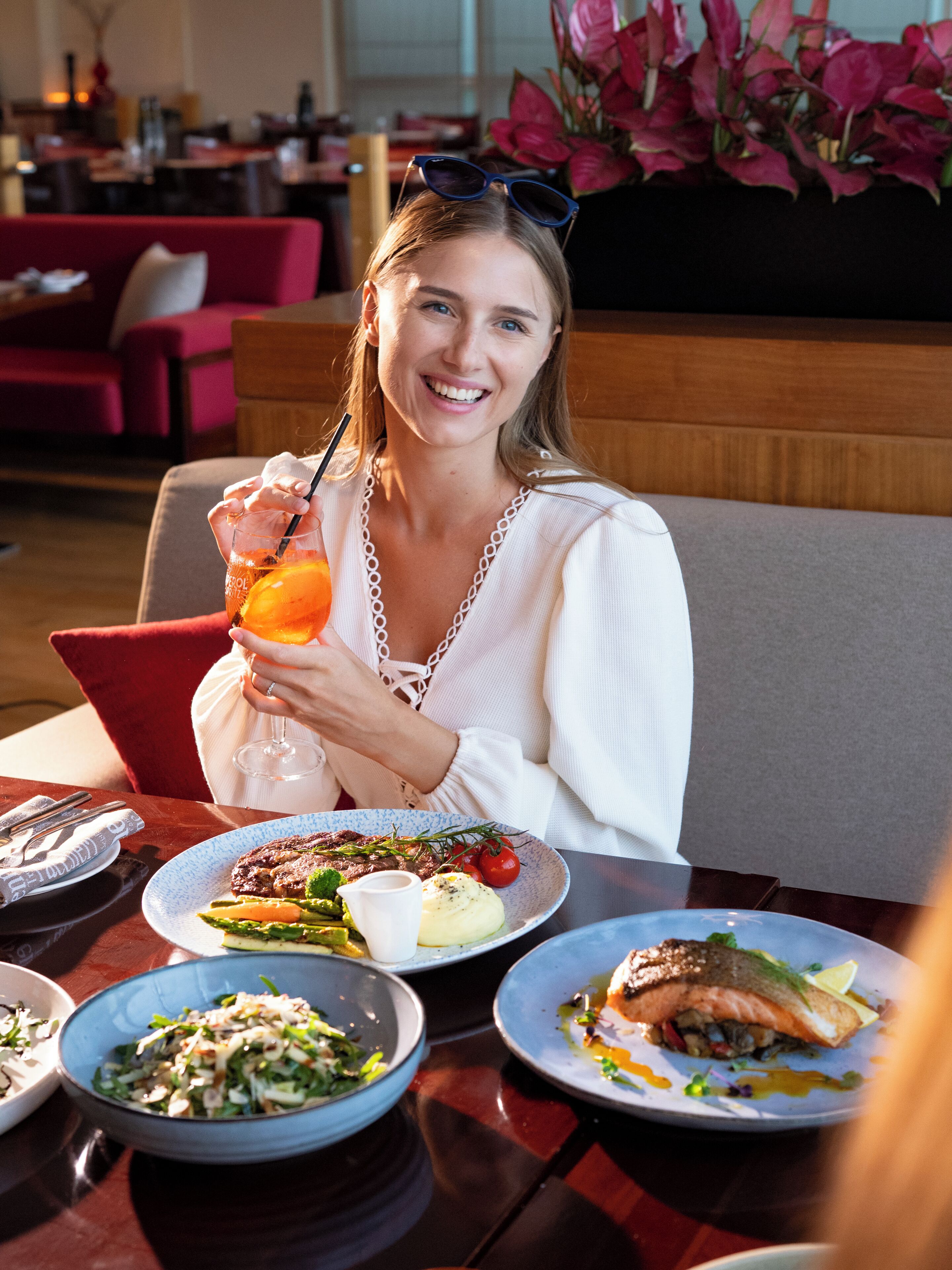 A person seated at a table with a meal, a drink, and a tablet.