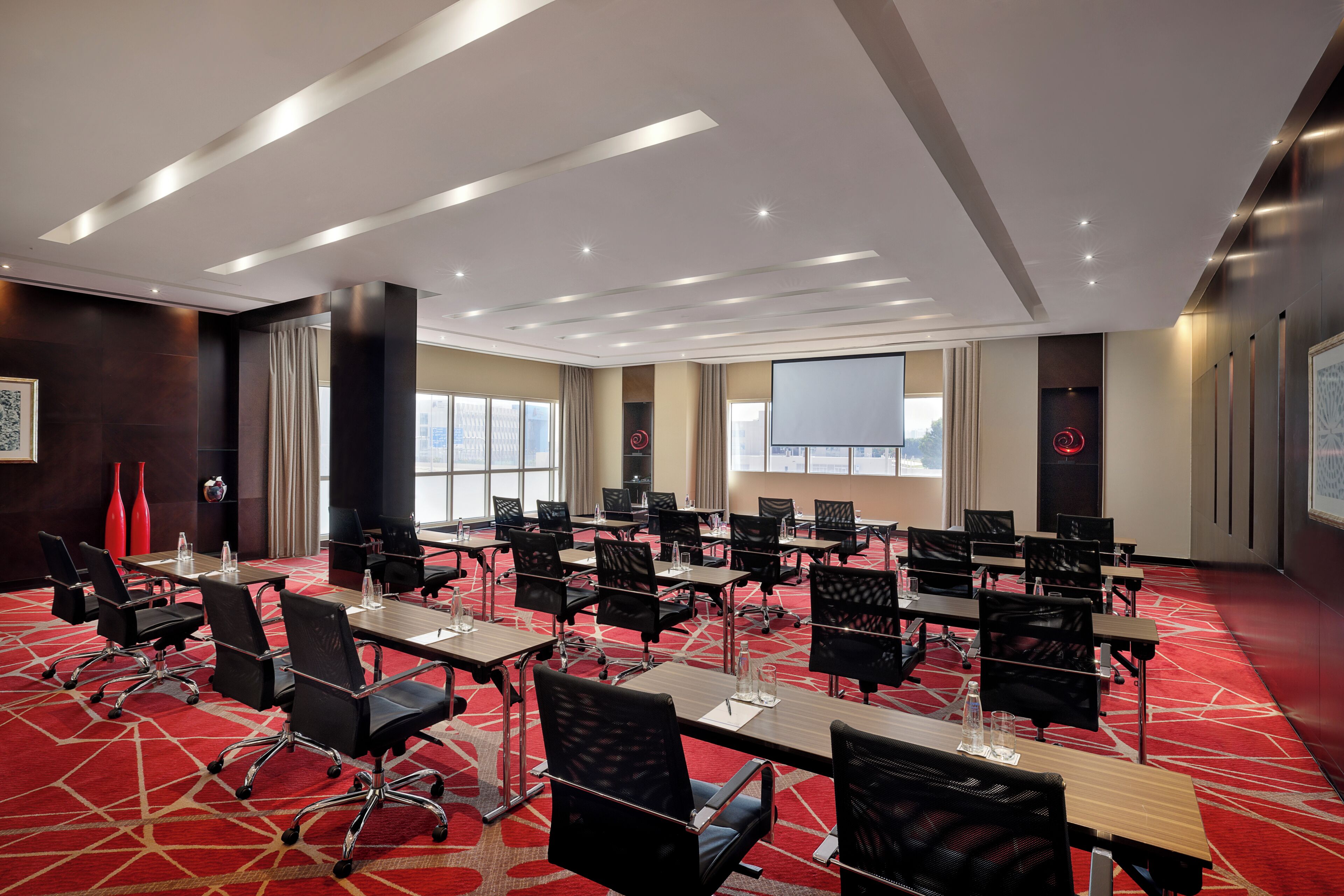 A conference room with multiple tables and chairs, large windows, and a red carpet.