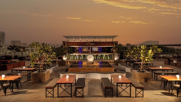 An outdoor dining area with tables and benches, a bar in the background, and a sunset sky. - Radisson Blu Hotel, Dubai Barsha Heights (Dubai)