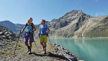 Two hikers on a rocky path with a mountain and lake in the background.