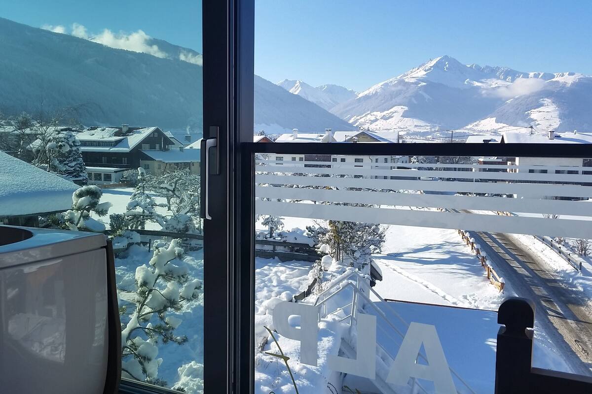 Vista desde una ventana sobre un paisaje nevado con montañas al fondo.