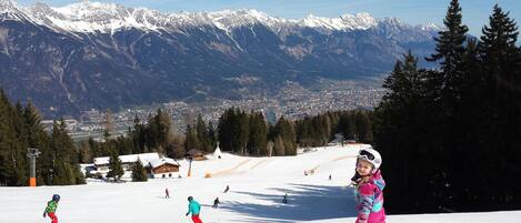 A ski resort with snow-covered slopes, a town in the background, and a mountain range.