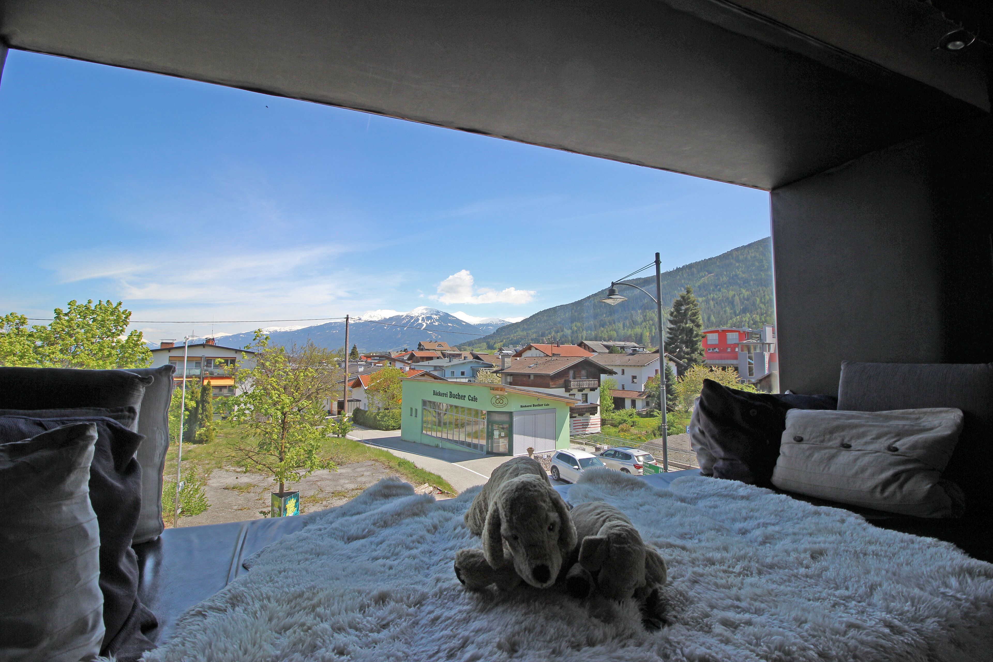 A bed with a view of a town and mountains.