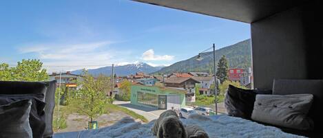 A bed with a view of a town and mountains.