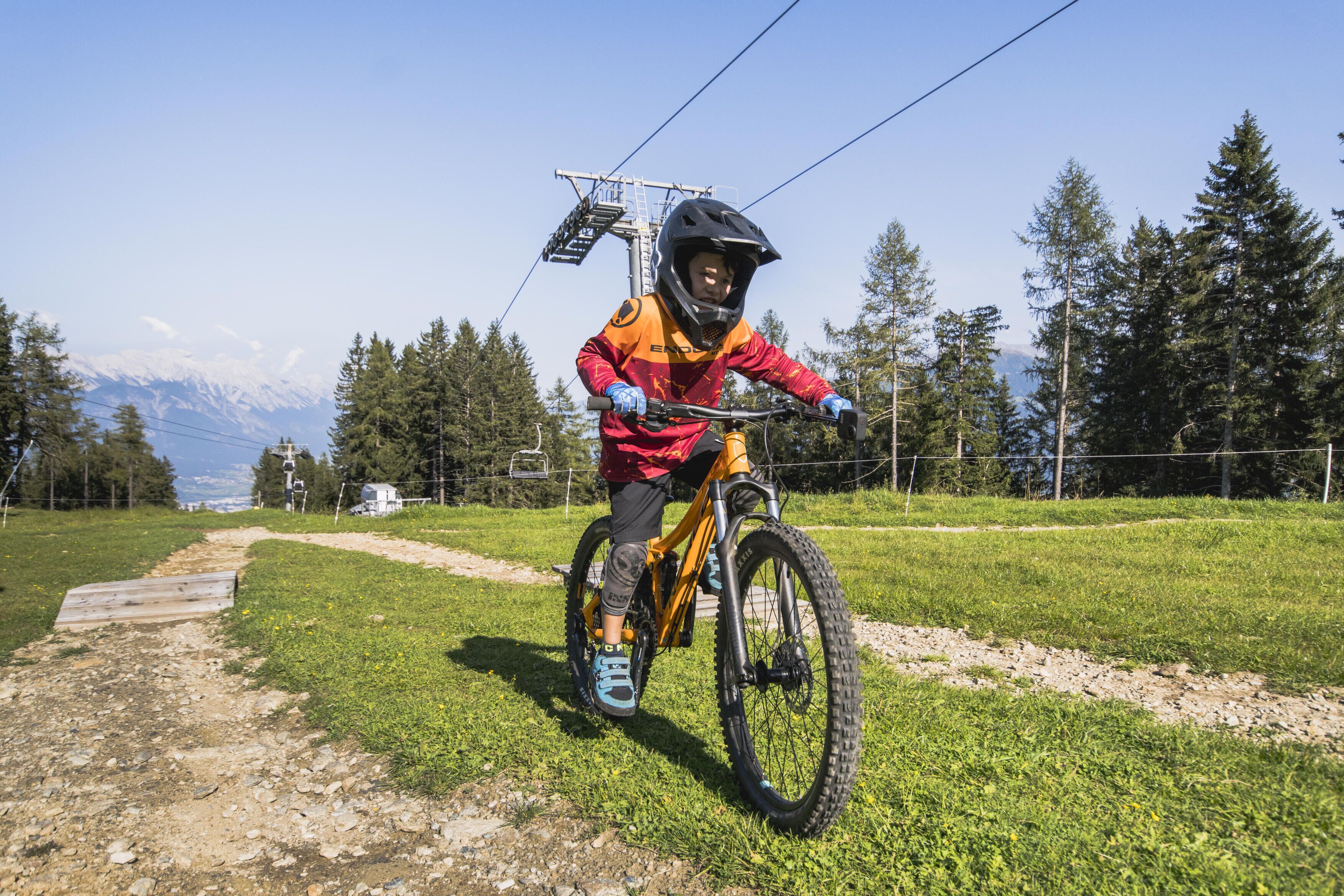 A person riding a mountain bike on a dirt path with a scenic view of mountains and trees in the background.