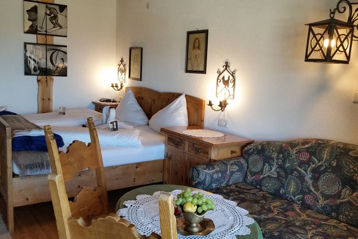 Una habitación acogedora con dos camas de madera, una silla de madera, un sofá estampado y una pequeña mesa con un frutero.