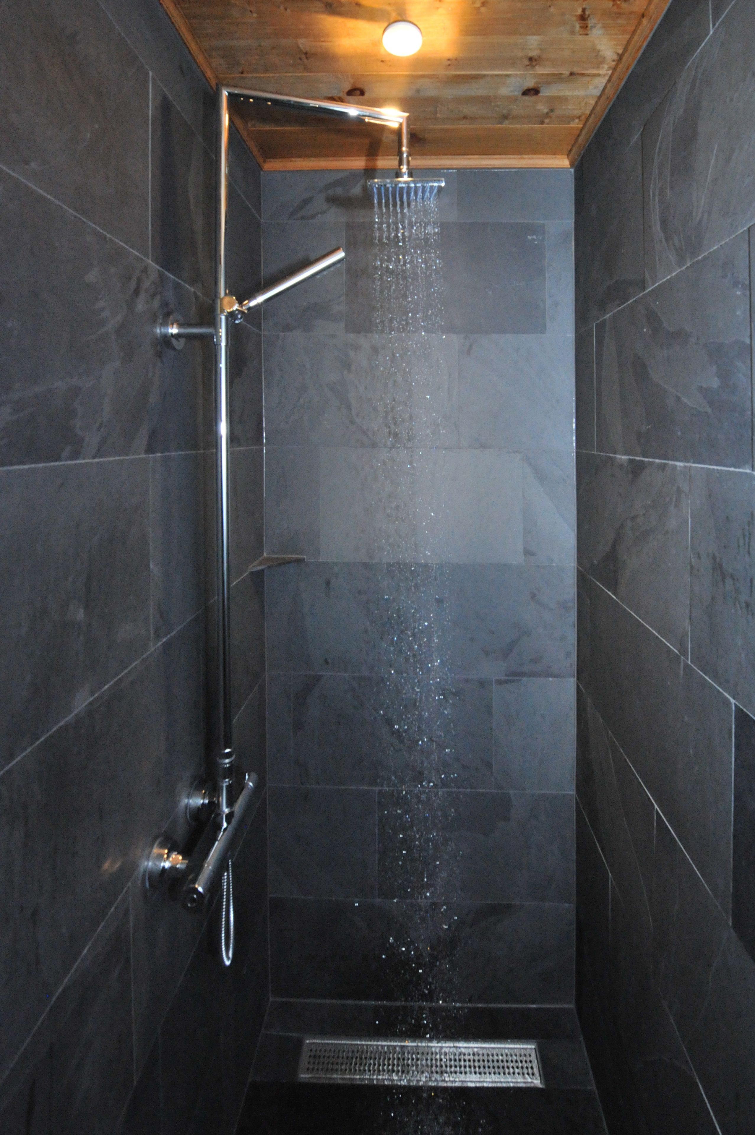 A modern shower with a rain showerhead, a handheld showerhead, and a drain.