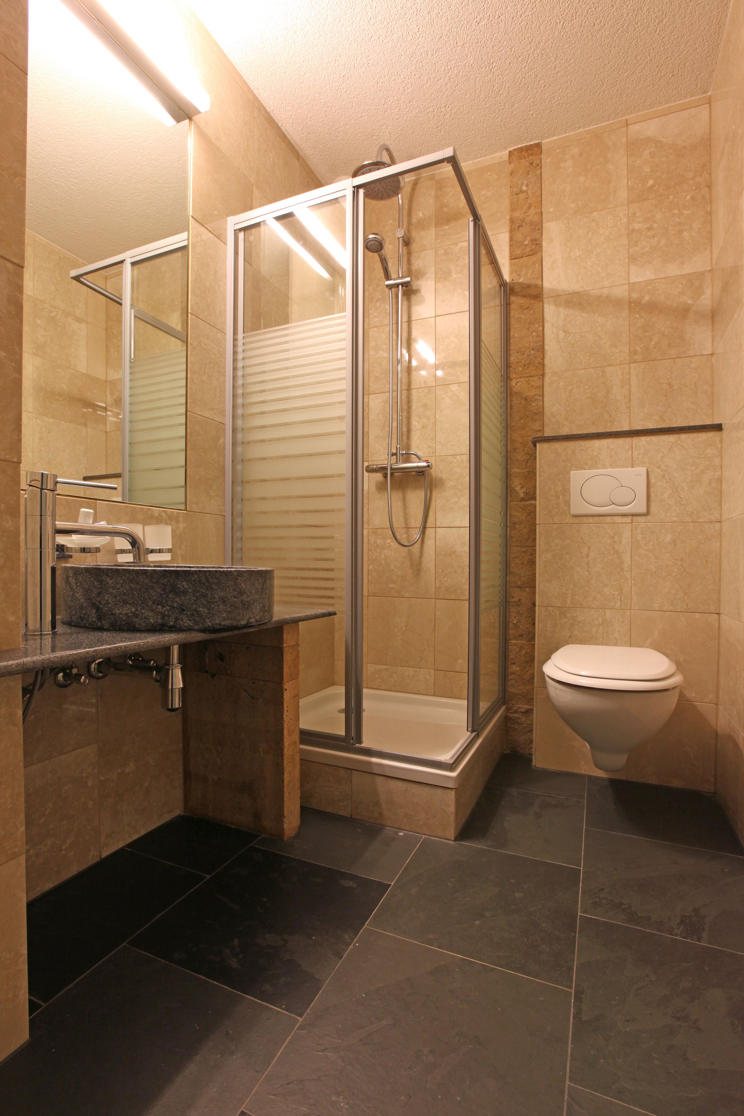 Ein Badezimmer mit einer Glaskabine zur Dusche, einem Waschbecken mit Marmorplatte und einer Toilette.