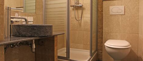 Ein Badezimmer mit einer Glaskabine zur Dusche, einem Waschbecken mit Marmorplatte und einer Toilette.