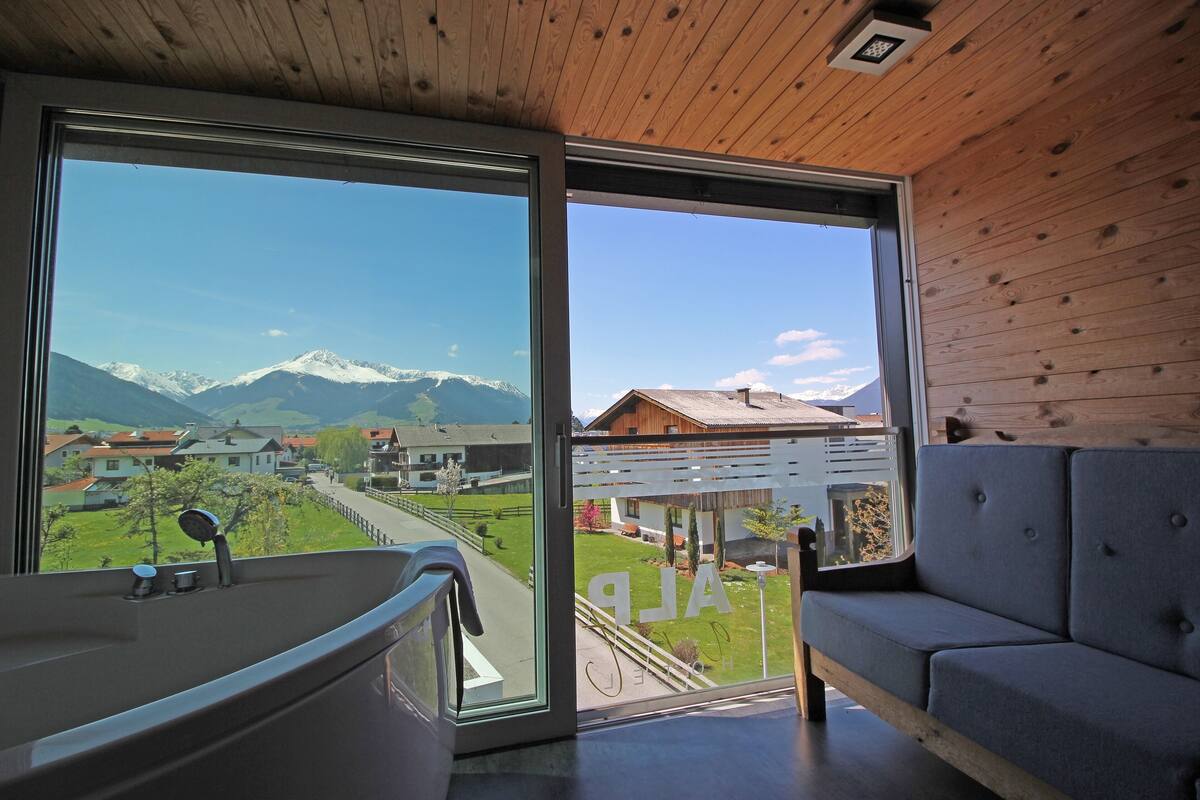 Una habitación moderna con un ventanal grande, una bañera y un sofá gris.