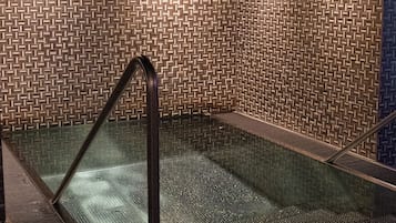 A glass-enclosed hot tub with a textured wall pattern, metal railings, and a ceiling with recessed lighting.