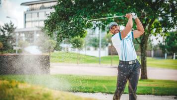 A golfer in mid-swing on a golf course with a building in the background.
