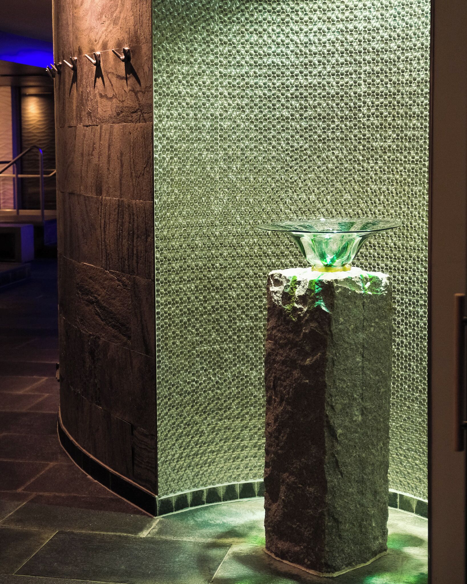 Un baño moderno con una columna de piedra, pared texturizada y lavamanos de cristal.