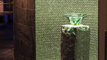 Un baño moderno con una columna de piedra, pared texturizada y lavamanos de cristal.