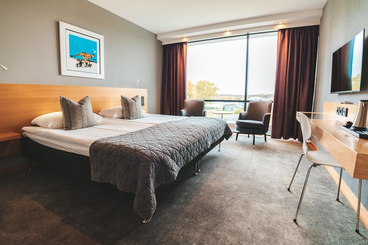 A hotel room with a large bed, a desk, a chair, a TV, and a window with curtains.
