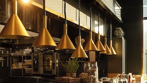 Una cocina con múltiples lámparas colgantes, electrodomésticos de acero inoxidable y diversos alimentos expuestos en la encimera.