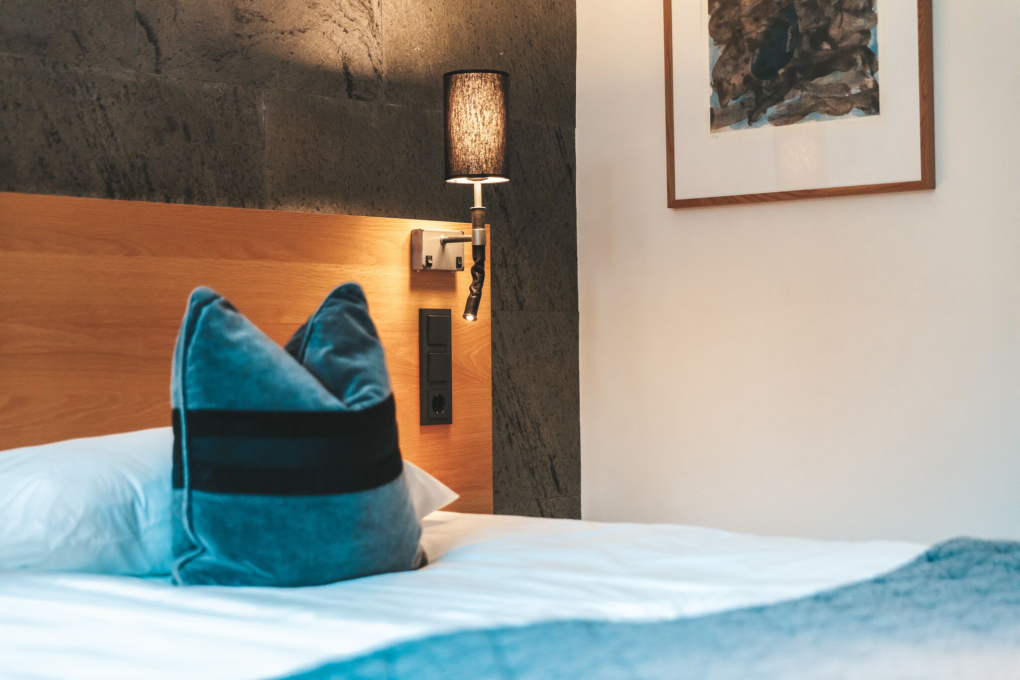 A neatly made bed with a blue pillow and a wooden headboard.