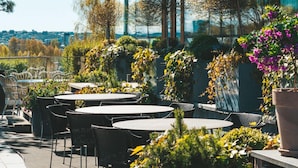 Un área de estar al aire libre con mesas y sillas redondas, rodeada de plantas y flores en macetas.