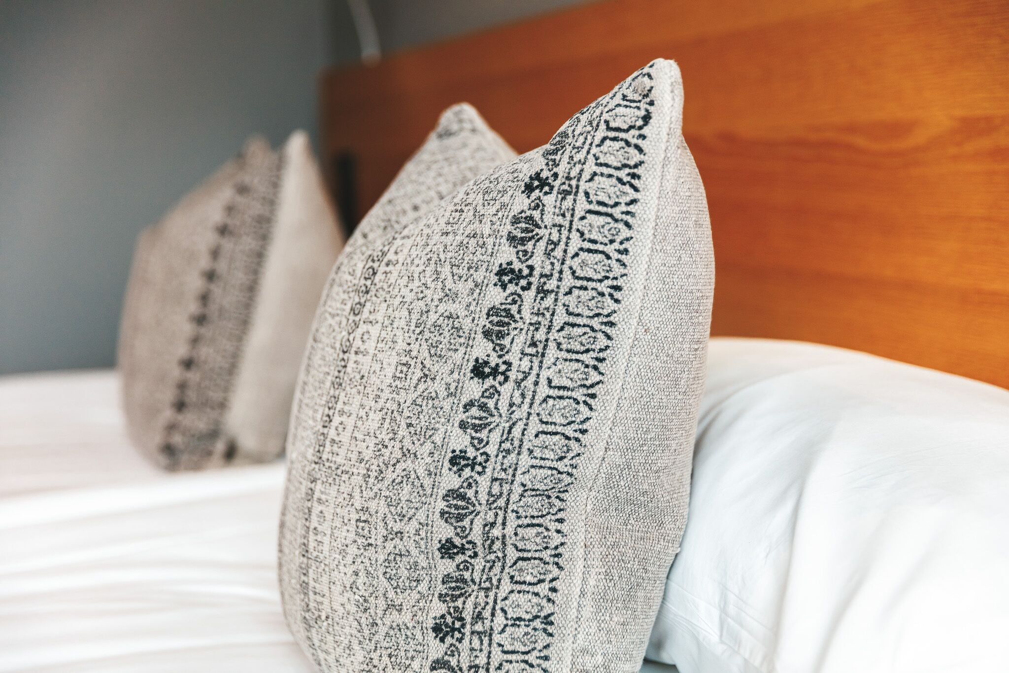 Primer plano de una cama con ropa blanca y almohadones decorativos con textura.