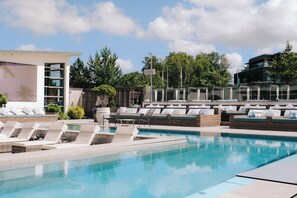 Un espace piscine comprenant des chaises longues, une petite piscine et un bâtiment à l’architecture moderne.