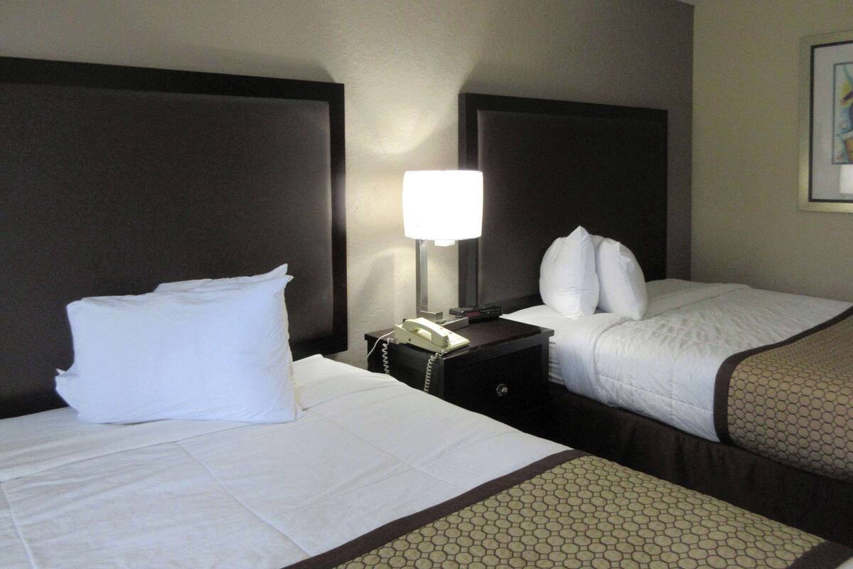 A hotel room with two beds, a nightstand with a lamp, and a telephone.