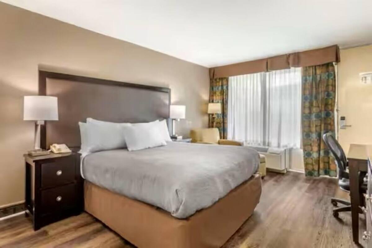 A hotel room with a large bed, two bedside tables with lamps, a chair, a desk, and a window with curtains.