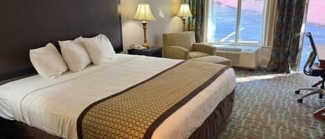 A hotel room with a large bed, two bedside lamps, a chair, and a view of the outdoors through a window.