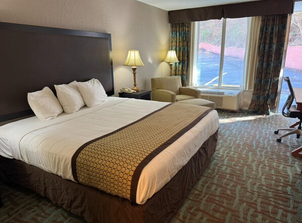 Habitación de hotel con una cama grande, dos lámparas de noche, una silla y vistas al exterior a través de una ventana.