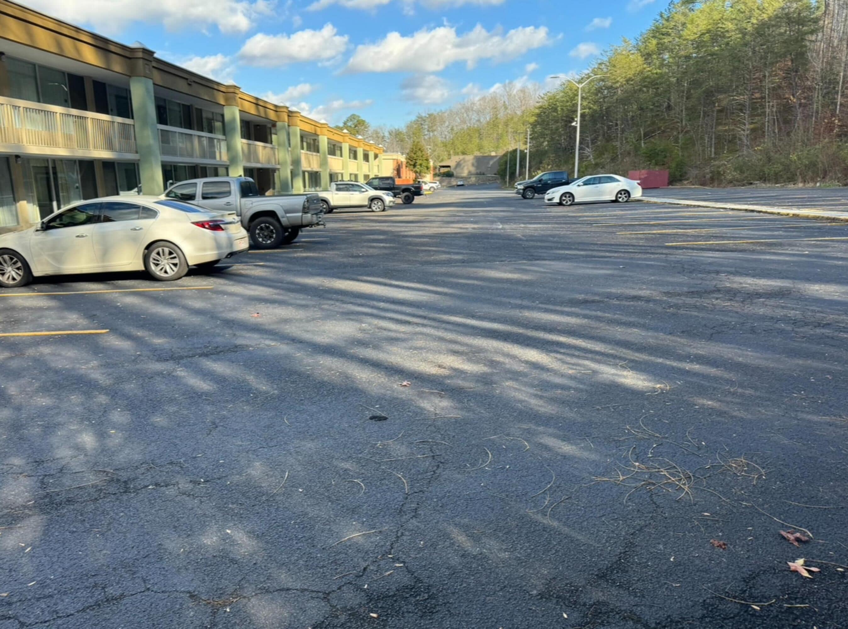 A parking lot with several cars and a building with multiple floors and large windows.