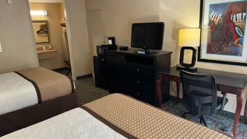 A hotel room with two beds, a desk with a computer and a lamp, a television, and a framed picture on the wall.