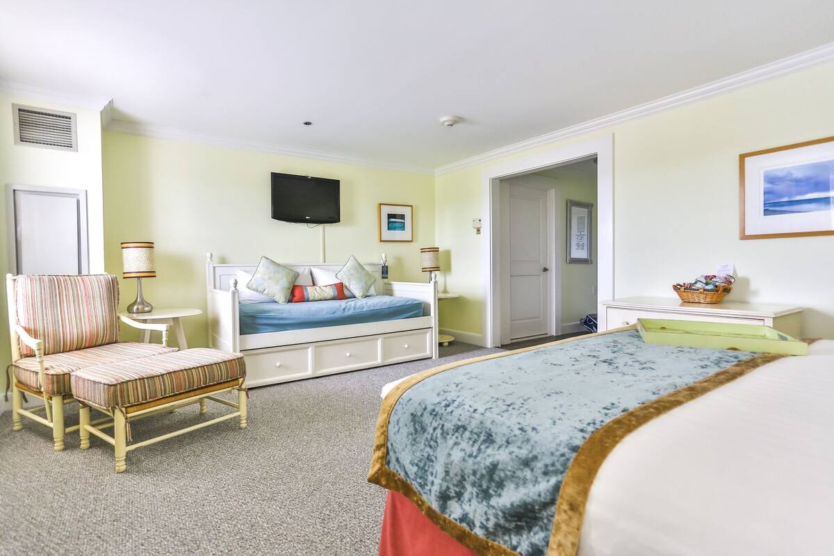 Ein Schlafzimmer mit Bett, Stuhl, Nachttisch, Lampe und Fernseher.