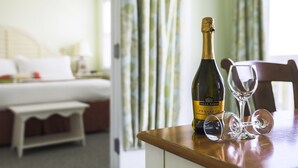 A hotel room with a bed, a bedside table with a bottle of Prosecco and two wine glasses. - Mansion House Inn And Spa (Vineyard Haven)