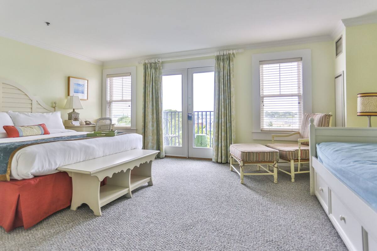 Ein Schlafzimmer mit Bett, Bank, Stuhl und einem Fenster mit Vorhängen.