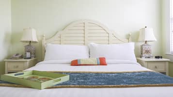 A neatly made bed with white linens, a blue textured throw blanket, and a green tray with a floral design. There are two bedside tables with lamps and a telephone on one.