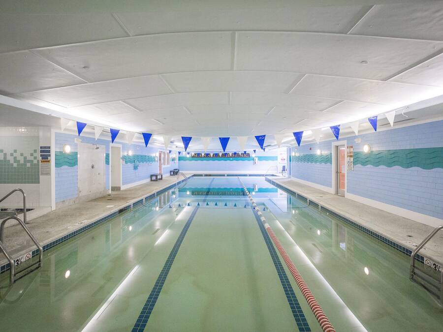 An indoor swimming pool with clear lane markings, tiled walls, and a ceiling with recessed lighting.