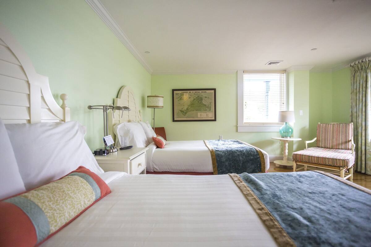 Ein Hotelzimmer mit zwei Betten, einem Schreibtisch, einem Sessel und einer Lampe, sowie einer Karte an der Wand.