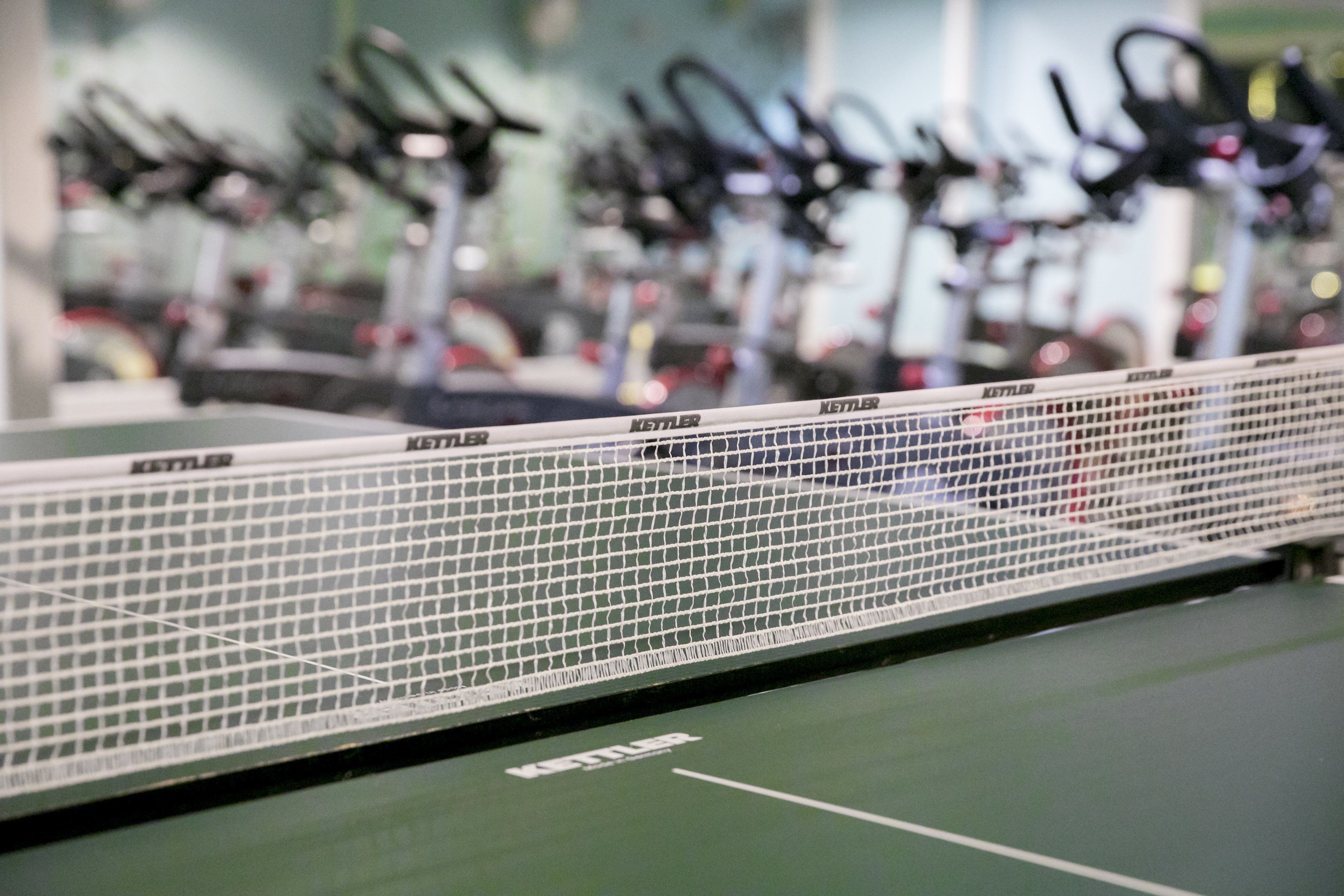 Una cancha de tenis con una red y varias bicicletas estáticas al fondo.