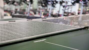 Una cancha de tenis con una red y varias bicicletas estáticas al fondo.