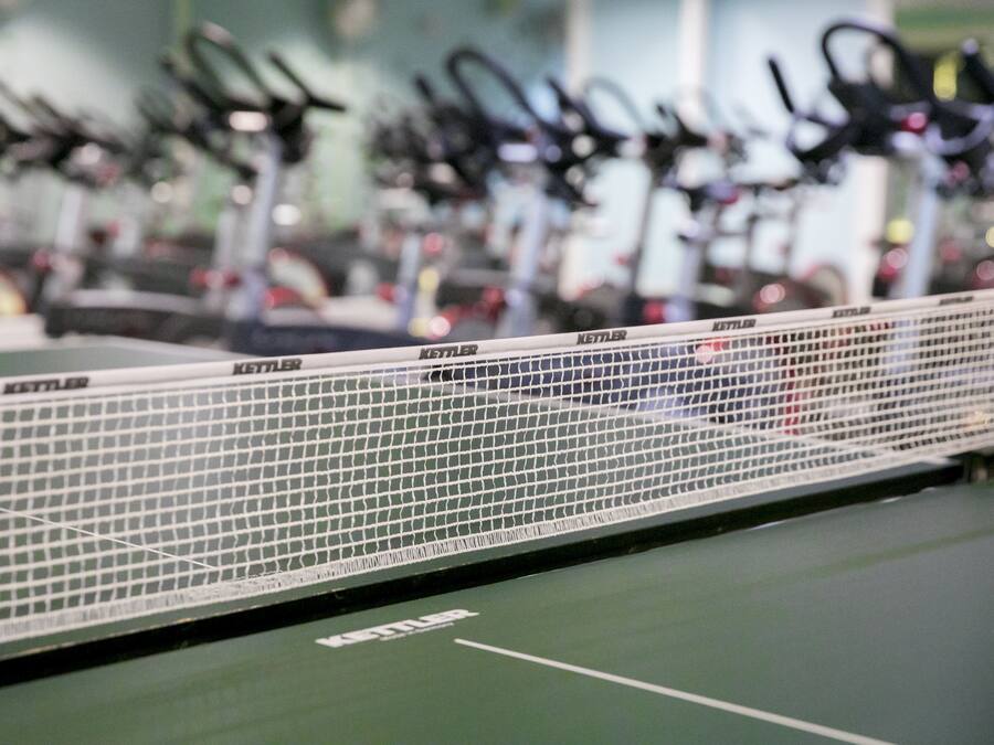 Una cancha de tenis con una red y varias bicicletas estáticas al fondo.
