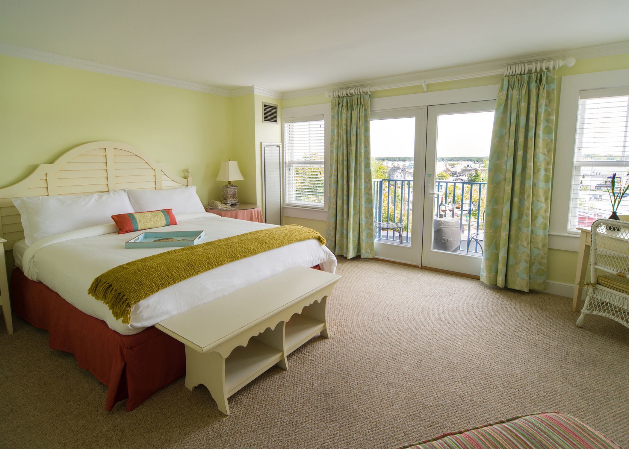 A hotel room with a large bed, a bedside table, a lamp, a window with curtains, and a balcony with a chair.