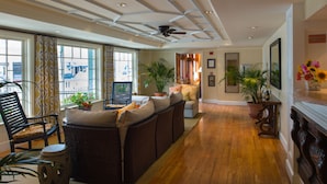 A spacious living room with a large sofa, a chair, and a small table. There are several potted plants and a ceiling fan. - Mansion House Inn And Spa (Vineyard Haven)