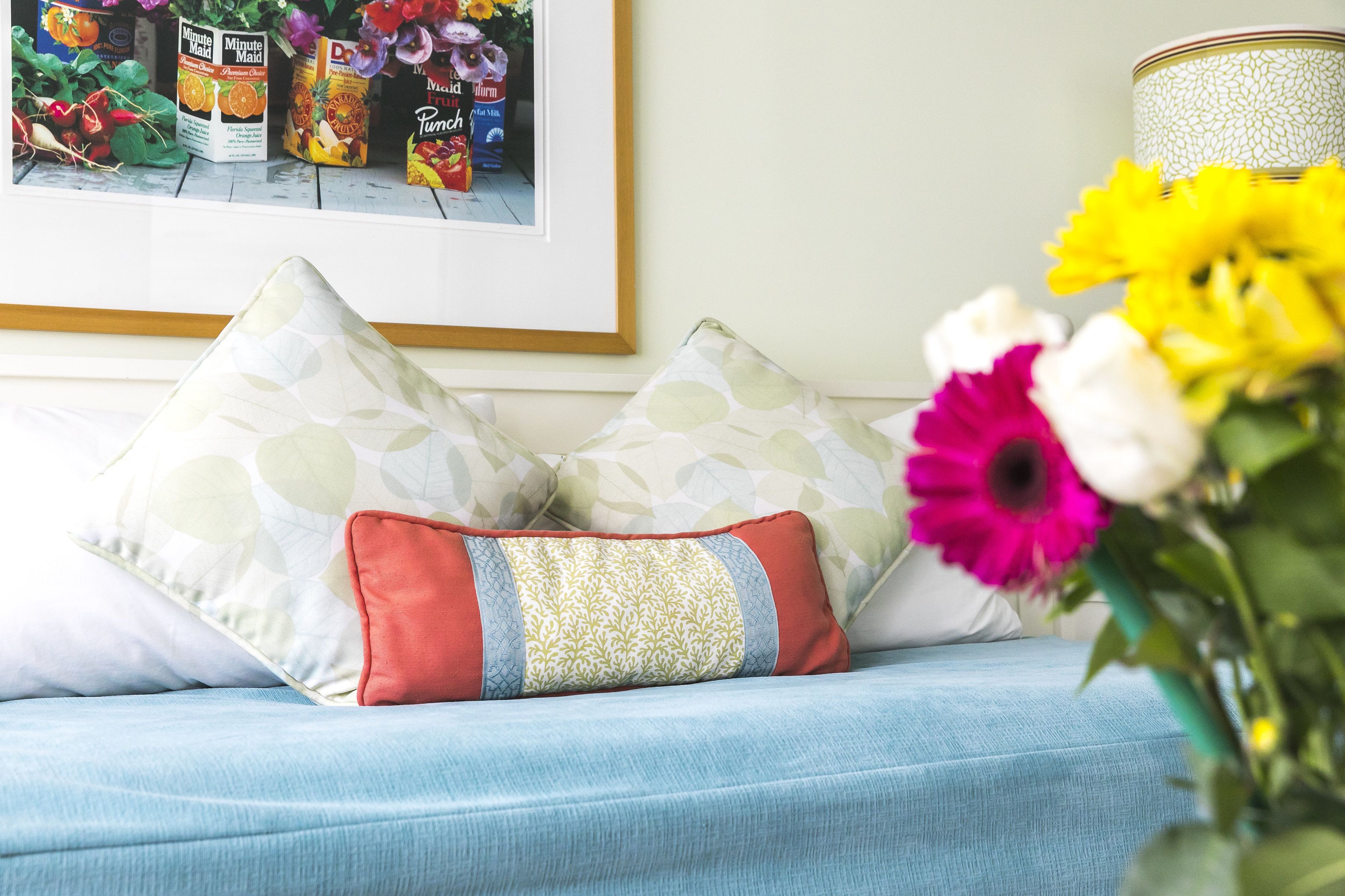 Ein Bett mit gemusterten Kissen, ein gerahmtes Bild von Lebensmitteln und eine Vase mit Blumen.